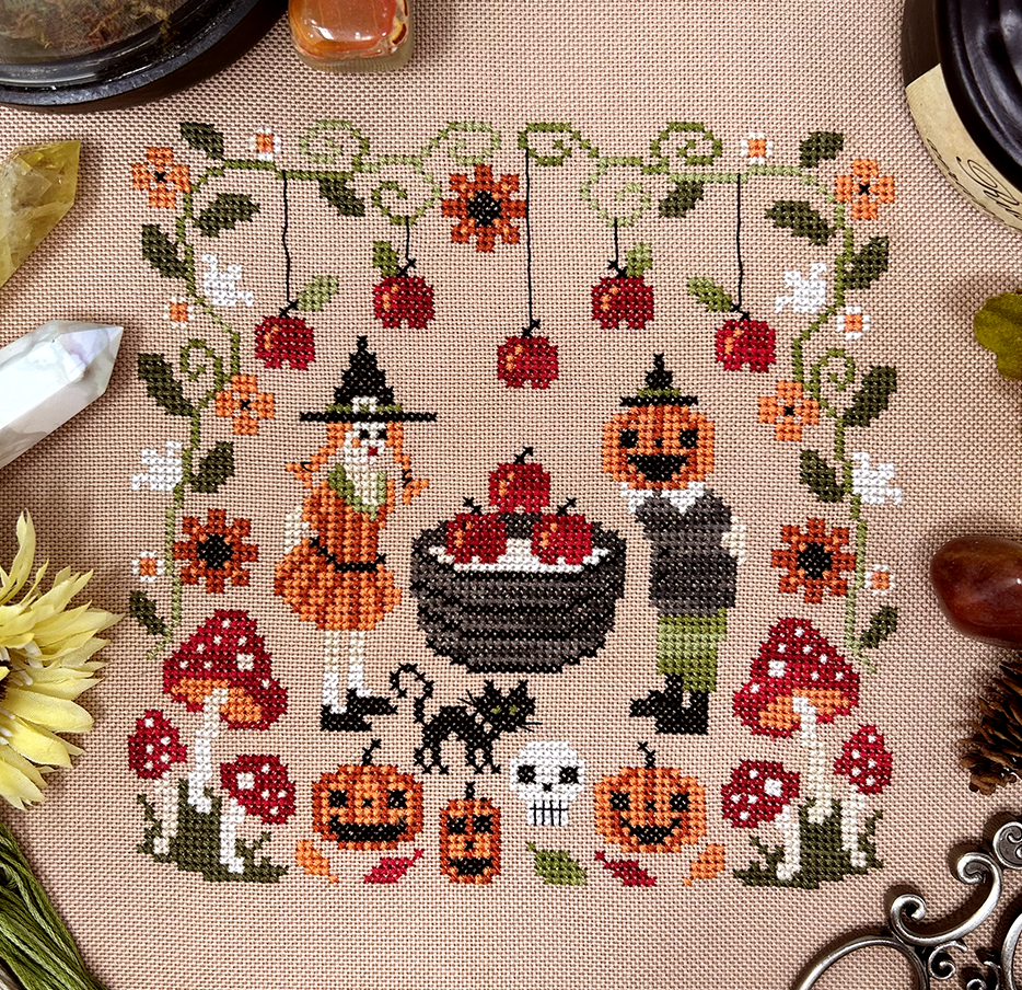 seasonal sampler with some cute characters about to bob for apples in a barrel, with a black cat, pumpkins, and vintage-inspired border. 
