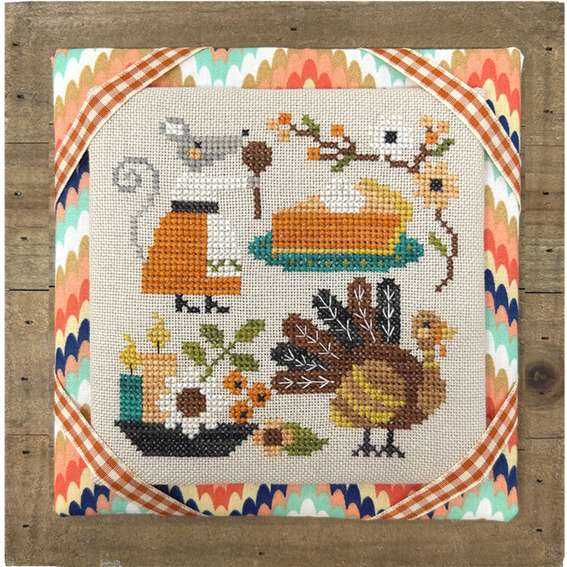 Cross-stitched design with a turkey, pie, and autumn elements on a wooden frame.